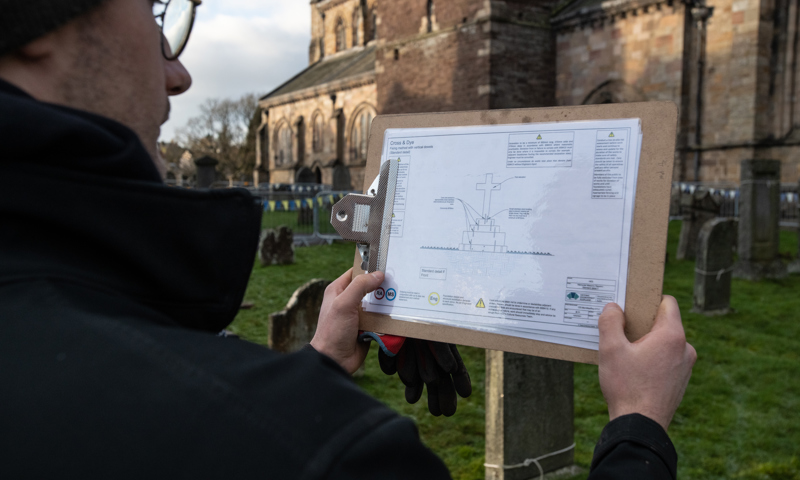 A person hold up a clipboard. On the clipboard is a diagram of the grave memorial.