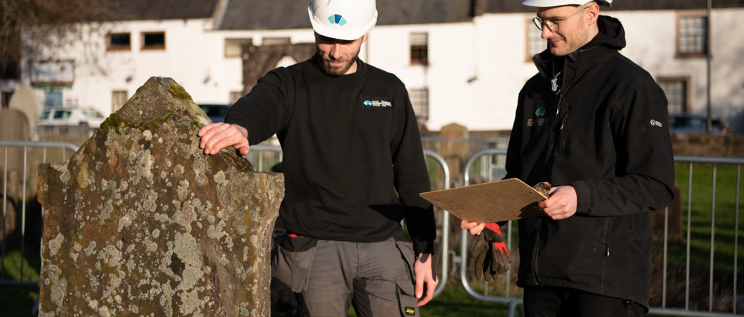 Two Historic Scotland staff member inspect a gravestone.