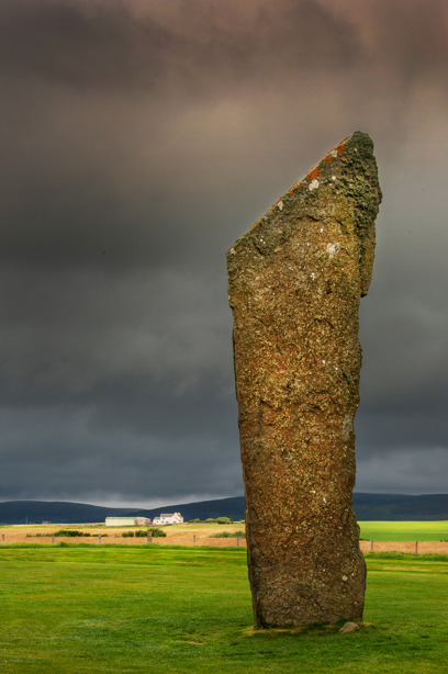 A tall, ancient standing stone in a field on a dark and stormy day