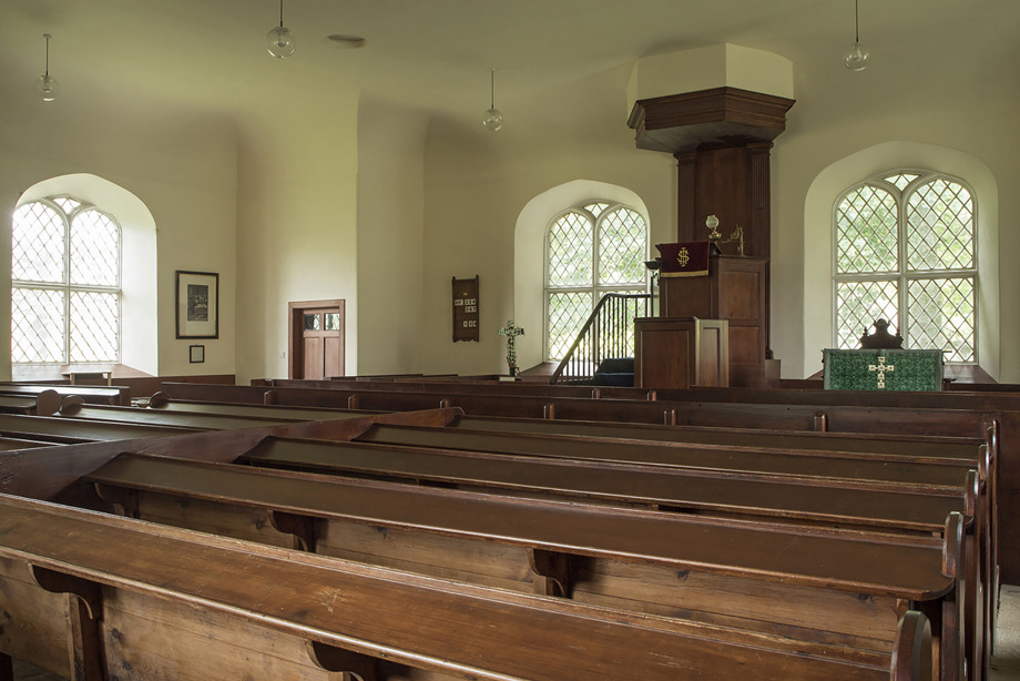 A row of wooden pews in a church with several arched windows. Image reference number 