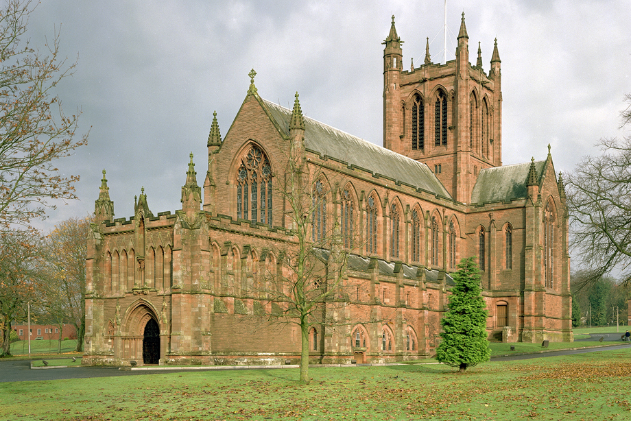 A large, historic stone church with lots of stone carving detail, in a countryside setting surrounded by grass.