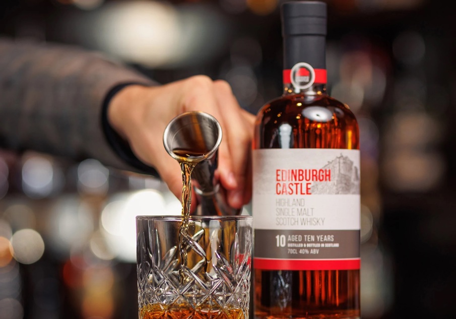 A bottle of Edinburgh Castle Single Malt Whisky and a measure of whisky being poured into a crystal glass