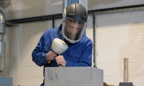 A photo of a stonemason in protective gear working on a stone. 