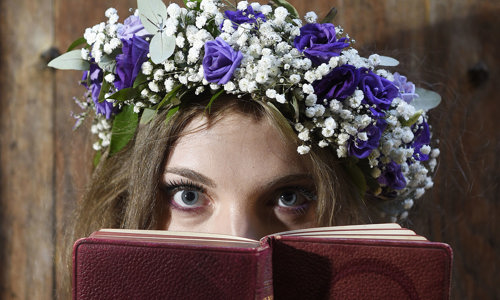 Midsummer fairy actor with flower headdress looks over a leather bound book