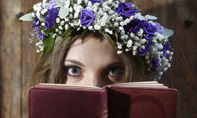 Midsummer fairy actor with flower headdress looks over a leather bound book