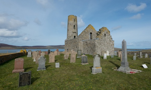 A photo of a church ruin by the sea with gravestones in the foreground. It's St Magnus Church, Egilsay, Orkney