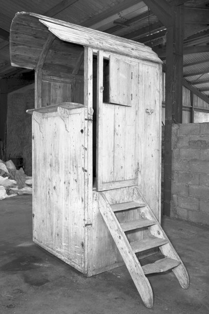 A tall, wooden stall with steps leading up to the entrance, and a curved roof over the top of the stall. There is a service hatch at the front. Image reference number: SC_400134