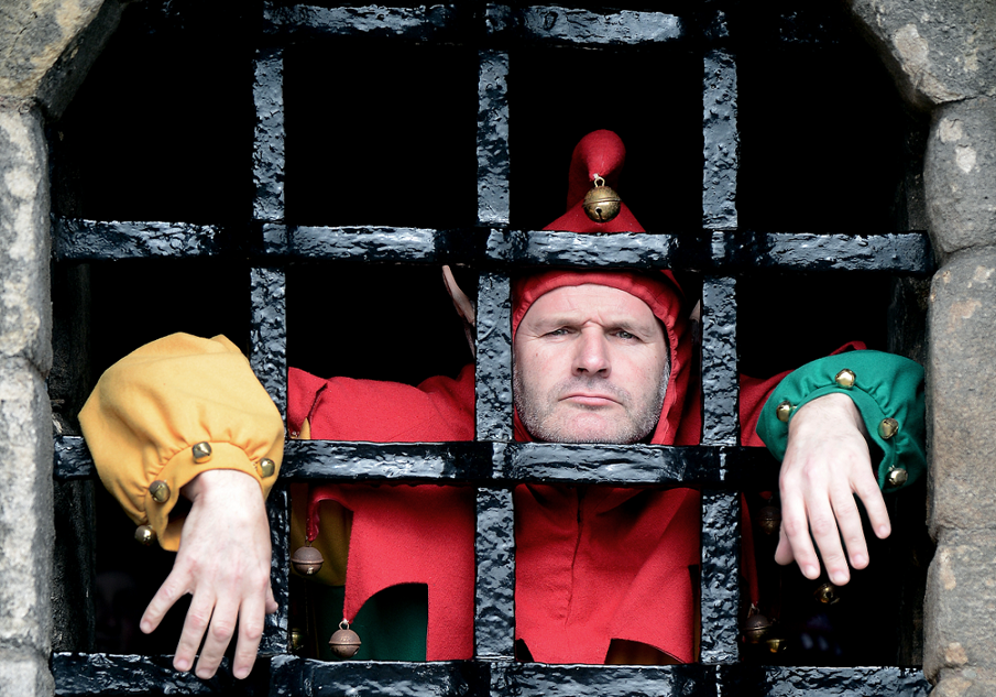 A costumed performer dressed as a jester and behind bars