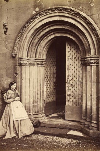 A visitor stands in front of a stone carved archway and knits