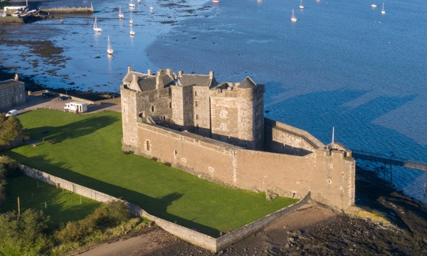 A historic castle with a large wall surrounding it, on the edge of an estuary 