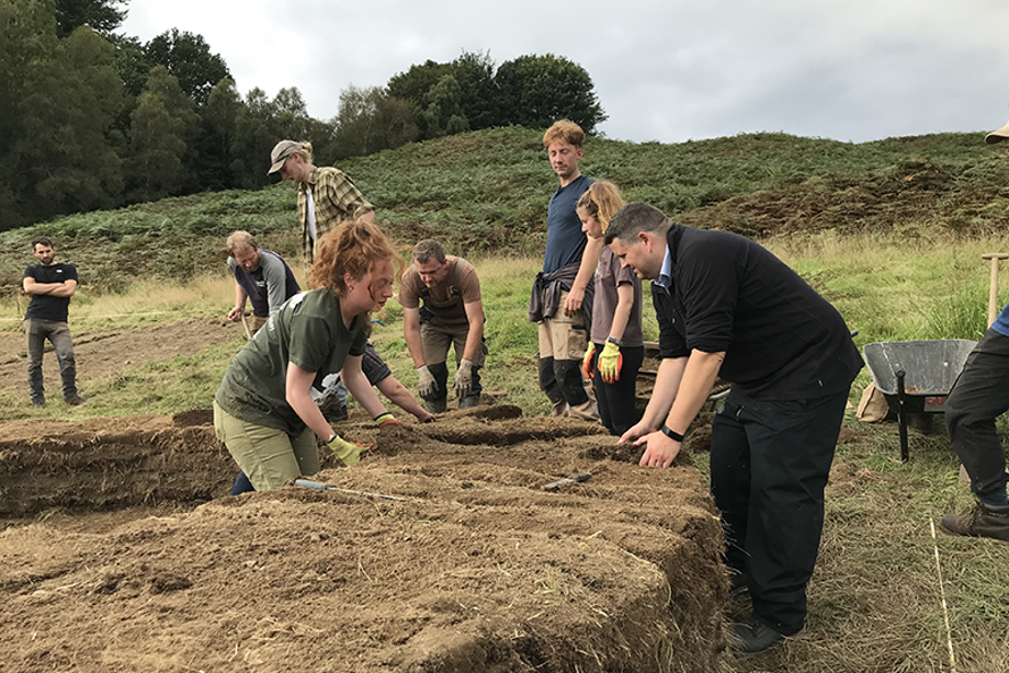 Seven people are in a field moving bales of hay and are surrounded by tools