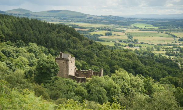 A well-preserved stone castle in a dramatic position at the head of a lush, tree-filled glen