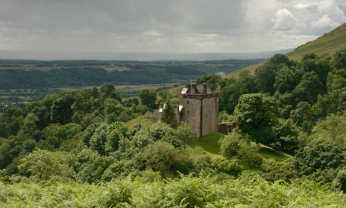 Castle Campbell seen from a distance, revealing its surrounding woodland and commanding view over the countryside.