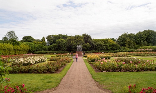 A landscape photo of the memorial garden showing all the flowers with two people looking at a statue