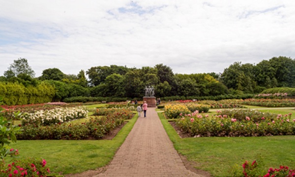 A landscape photo of the memorial garden showing all the flowers with two people looking at a statue