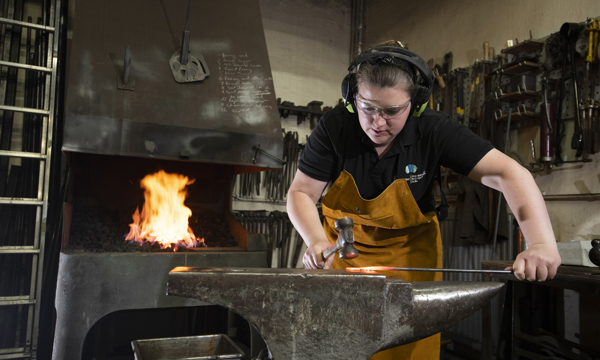  blacksmith working in front of a fire to forge a piece of steel by beating hot metal into shape on an anvil