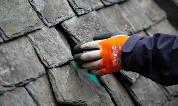 Someone's hand working on a traditional slate roof 