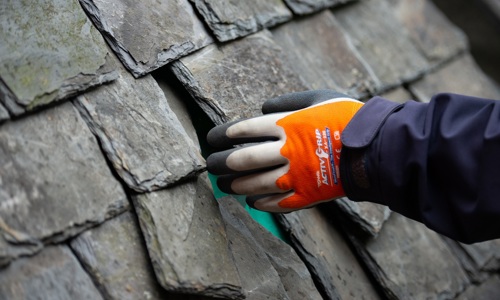 Someone's hand working on a traditional slate roof 