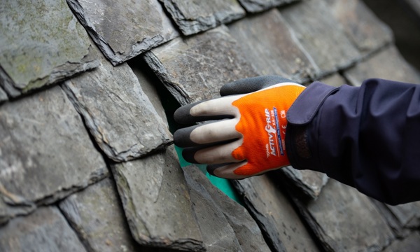 Someone's hand working on a traditional slate roof 