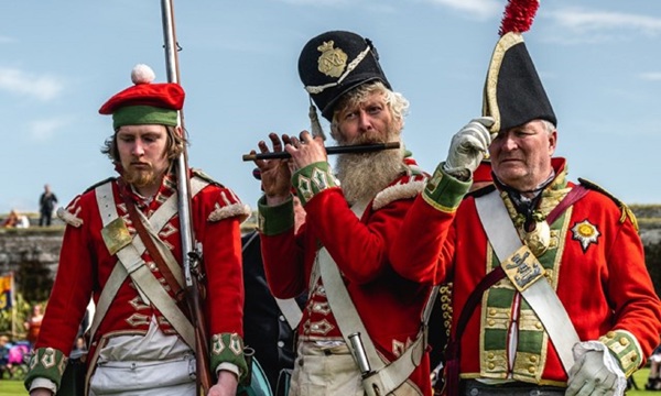 Three people standing in costume with the one in the middle playing a flute