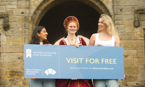 Three woman standing in front of a castle holding an oversized ticket