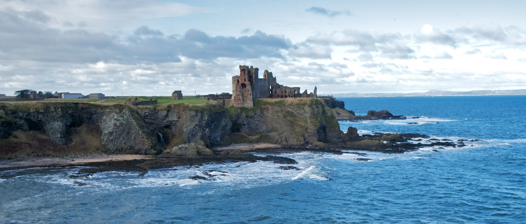 A castle on the edge of a cliff with water smashing against the rocks 