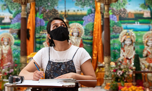 A woman wearing a face mask looking around the building she is in looking for inspiration for her sketches