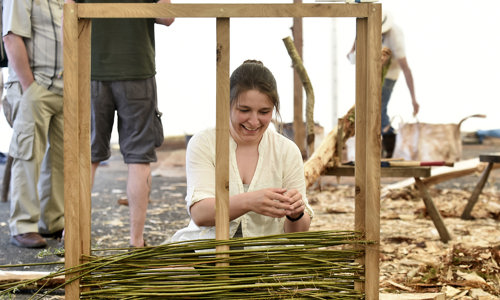 A woman sitting in front of a wooden frame adding bamboo 