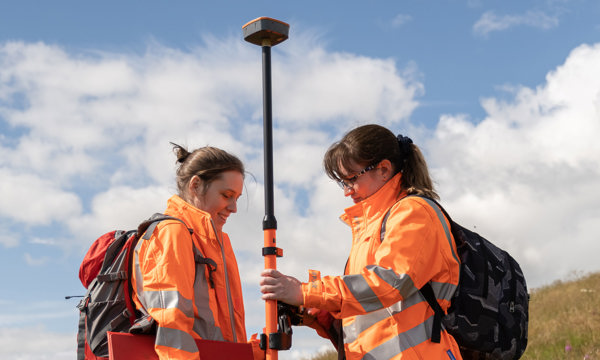 Two women in orange high vis jackets wearing ruck sacks 