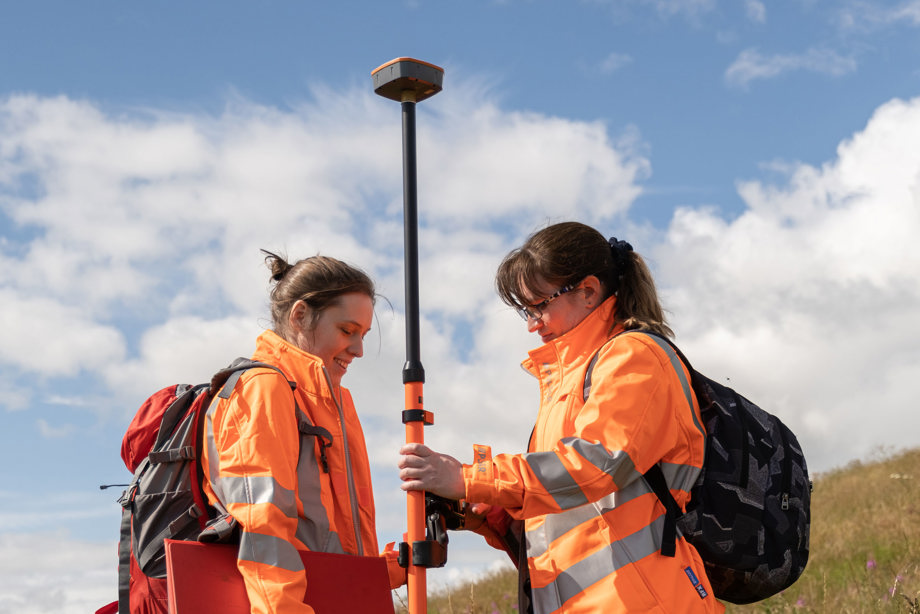 Two women in orange high vis jackets wearing ruck sacks 