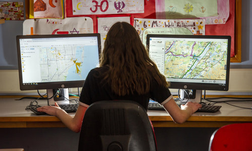 A woman with long hair working on two computer monitors