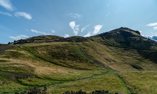 A photo of Arthur's Seat with blue skies in the background