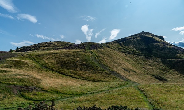 A photo of Arthur's Seat with blue skies in the background