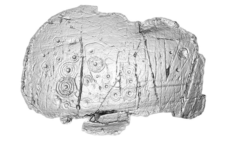 Image is a grey metallic looking picture of a stone, rendered in 3D. The concentric circular carvings stand out on the surface of the stone.