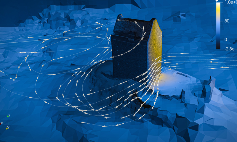 Image is a computer-generated simulation of wind blowing around a large tower. The image depicts the wind flow as a series of white arrows, moving around the sides of the stone tower, with a windspeed gauge in the top right of the picture.