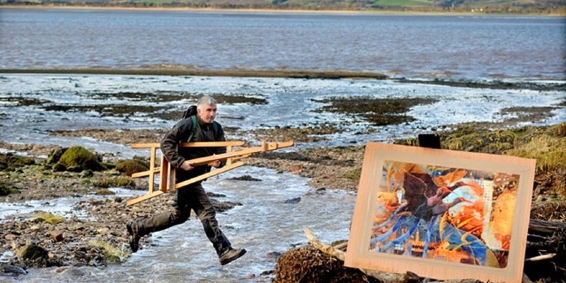 Artist Derek Robertson on a beach background with one of his artworks