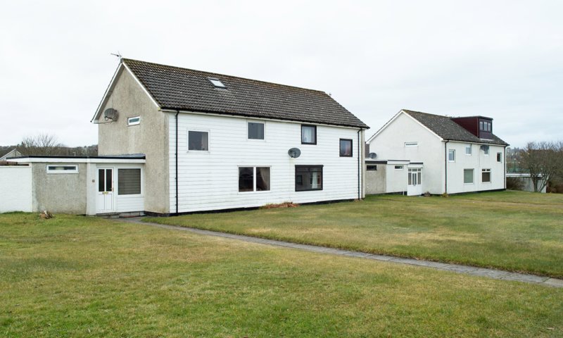 A pair of brick and timber semi-detached houses, with well-tended grass lawns in front. The buildings are grey sided and have white timbered frontages.
