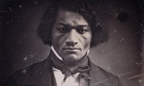 A very early era black and white photograph of a person intently staring at the camera. They are wearing a suit jacket and waistcoat, with a white shirt and cravat.
