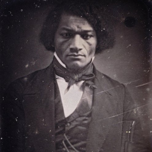 A very early era black and white photograph of a person intently staring at the camera. They are wearing a suit jacket and waistcoat, with a white shirt and cravat.