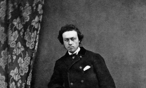 Black and white image of a man wearing formal attire of the mid 19th century, leaning on a lectern which has a closed book on it. 