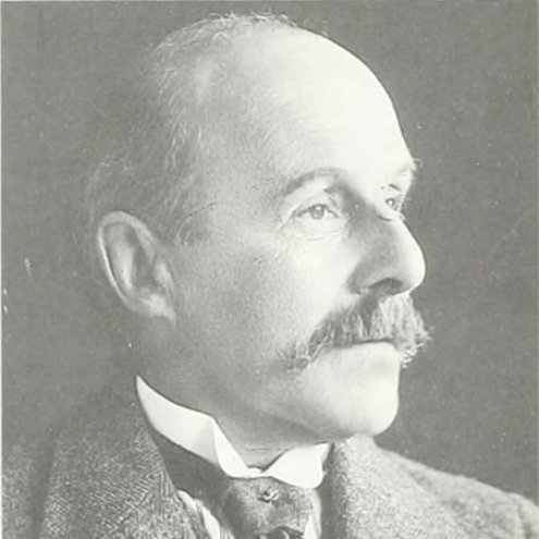 Black and white portrait photo of a person looking to the right of camera. They are wearing an old-style suit and thin tie, and have bushy hair around their ears.