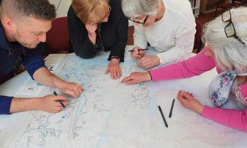 Four people leaning over a table with a map on it 