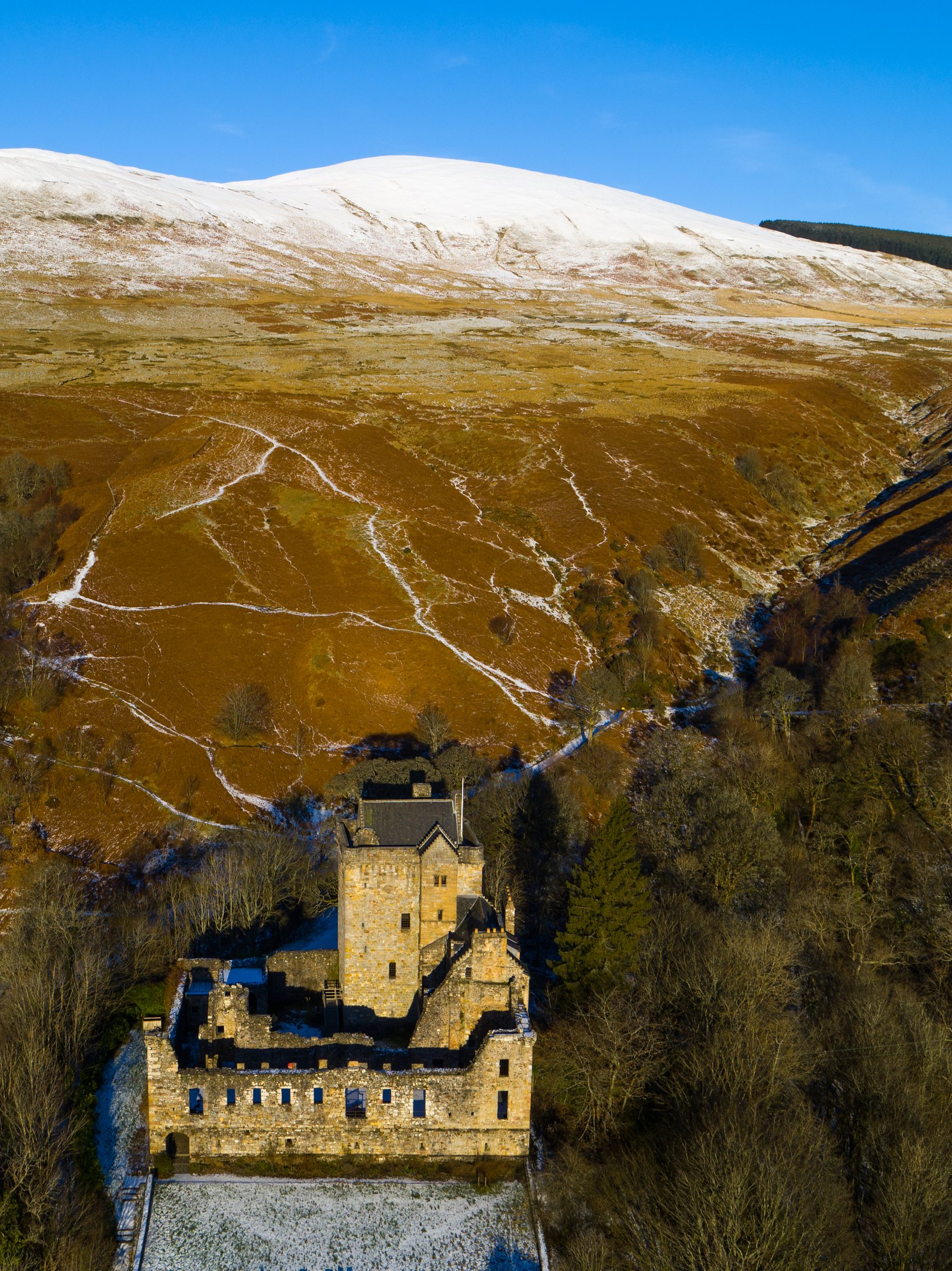 Portrait aerial view of Castle Campbell against the backdrop of snowy hills in the Dollar Glen. 