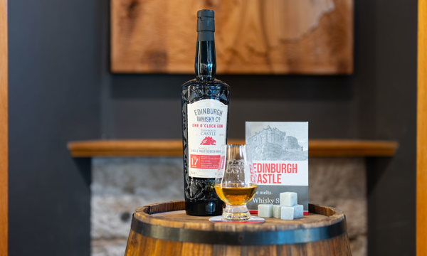 A bottle of One O'Clock Gun Whisky on a barrel with an Edinburgh Castle Whisky glass and Whisky Stone ice cubes