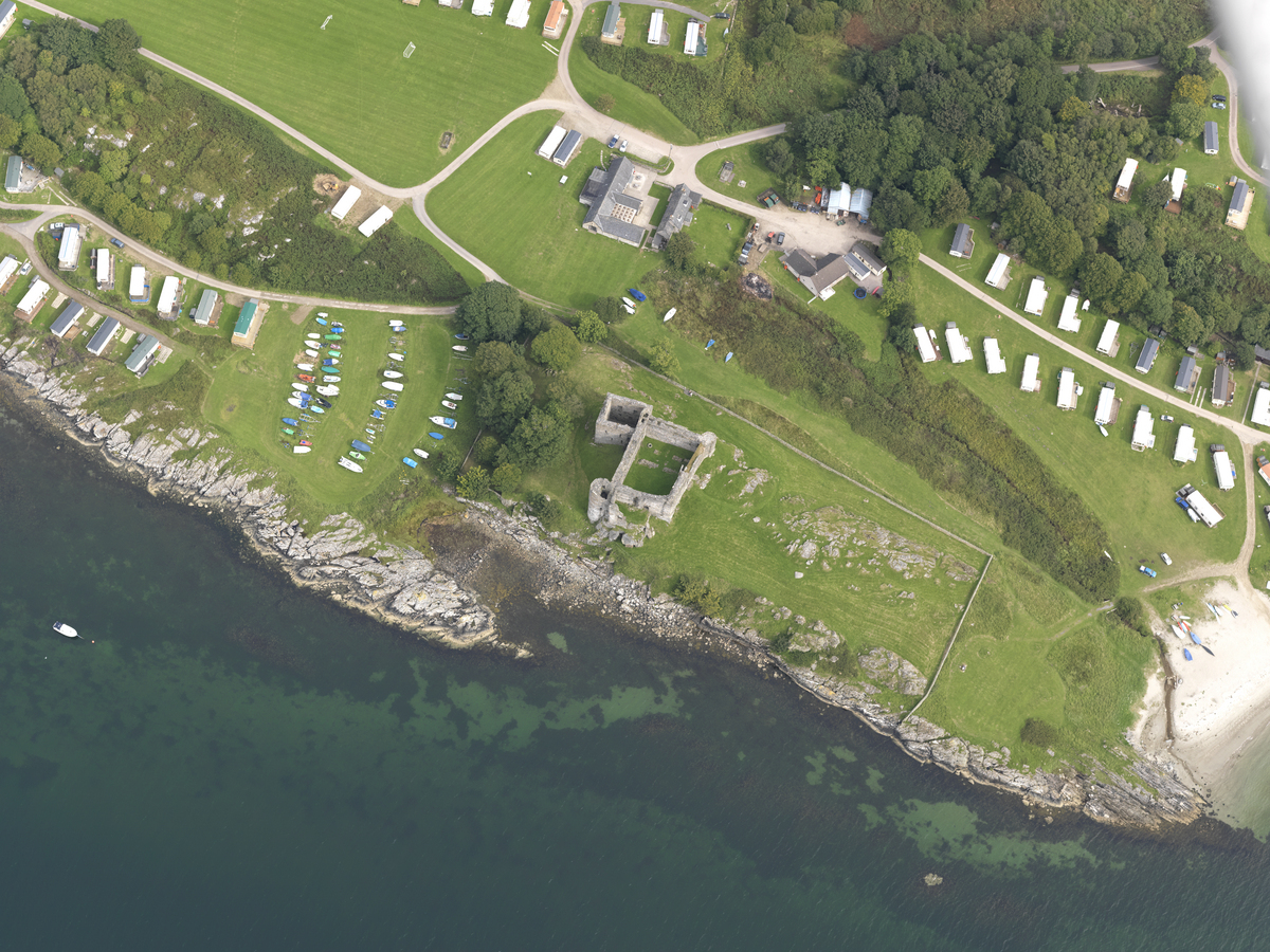 Aerial view of castle ruin beside coastline with caravan parks on either side