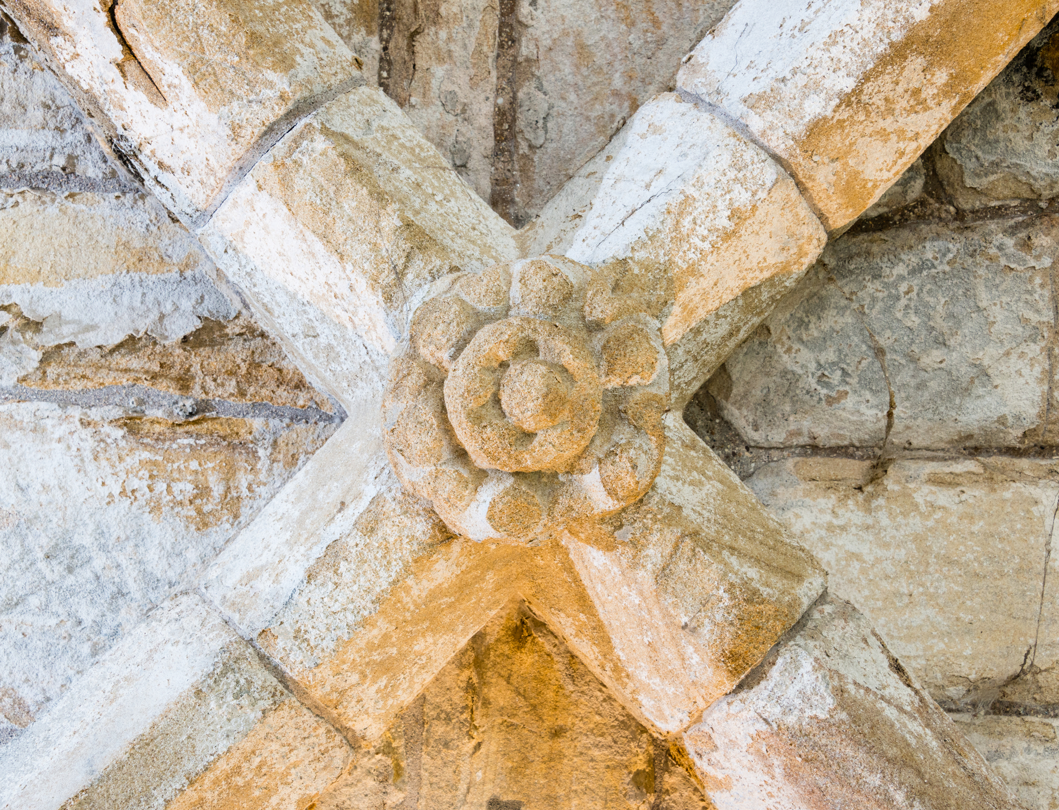 A close-up of an ornate carved stone boss on a ceiling, showing weathered but intricate craftsmanship.