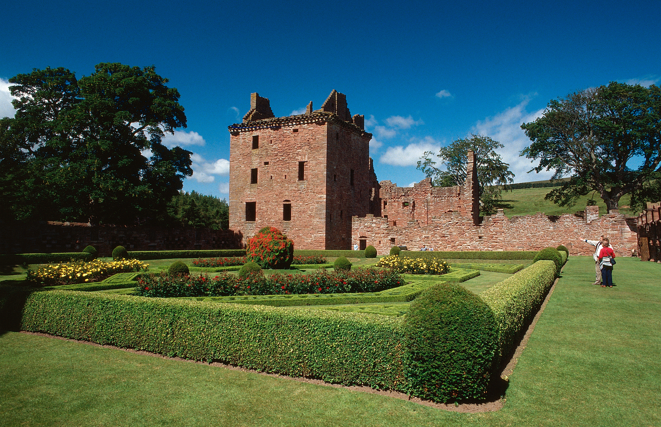 Visitors wander around the ornate walled gardens at Edzell Castle. The castle provides a dramatic backdrop to manicured lawns, hedges and flower beds. 
