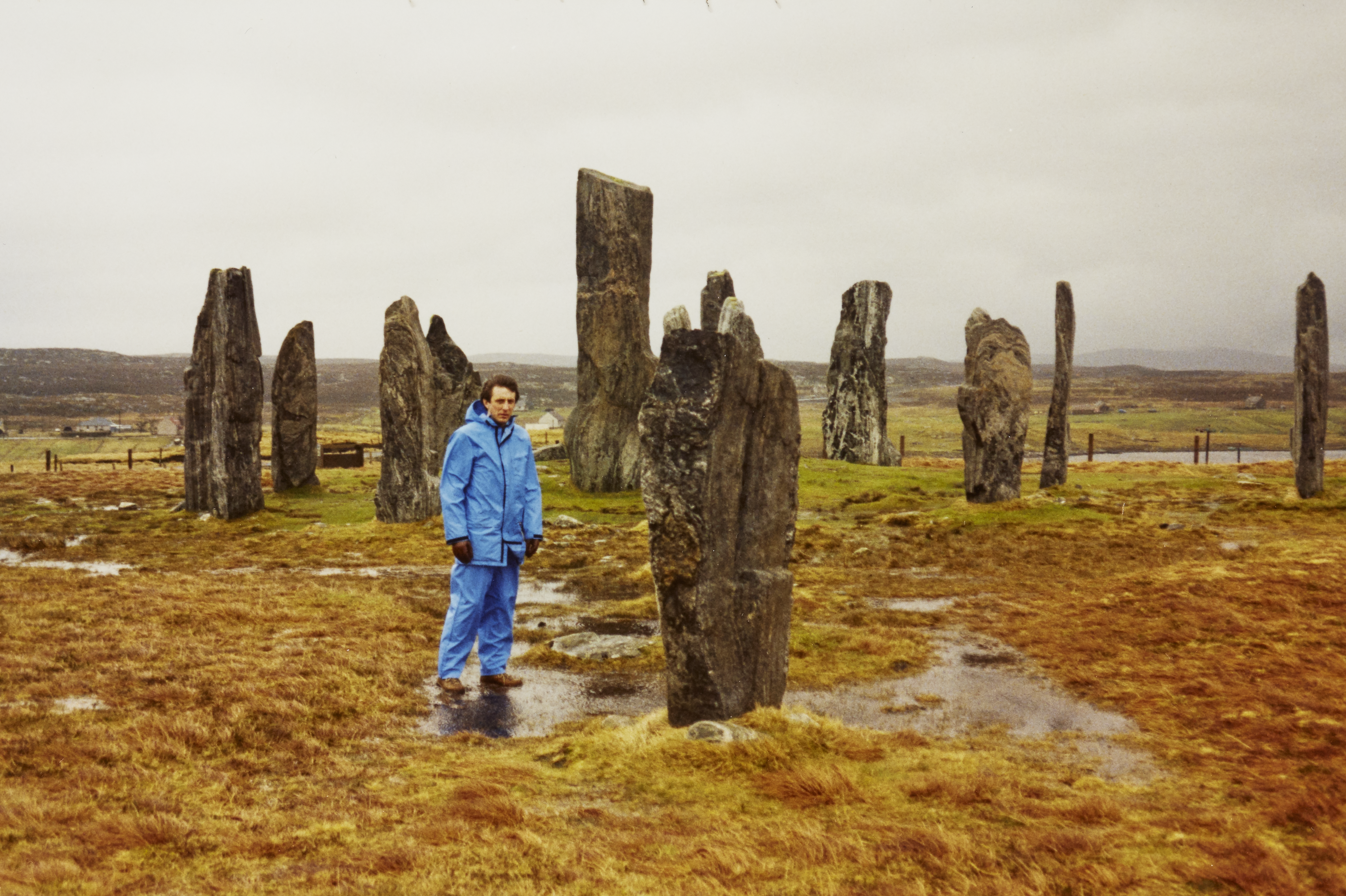 Person in blue clothing standing at the Calanais Standing Stones on a rainy day with big puddles