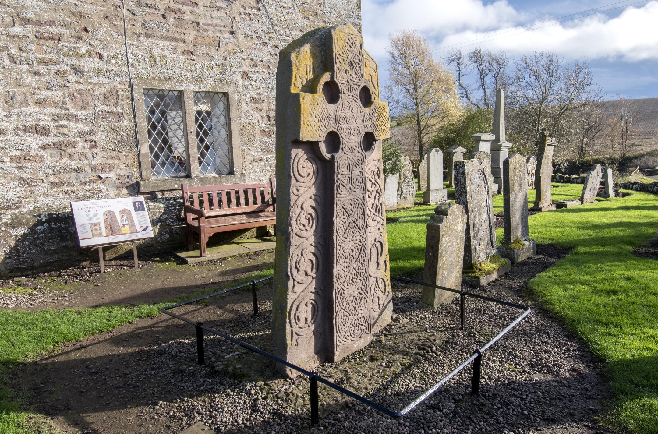 Sculptured stone bearing a cross shape in a graveyard with church wall behind