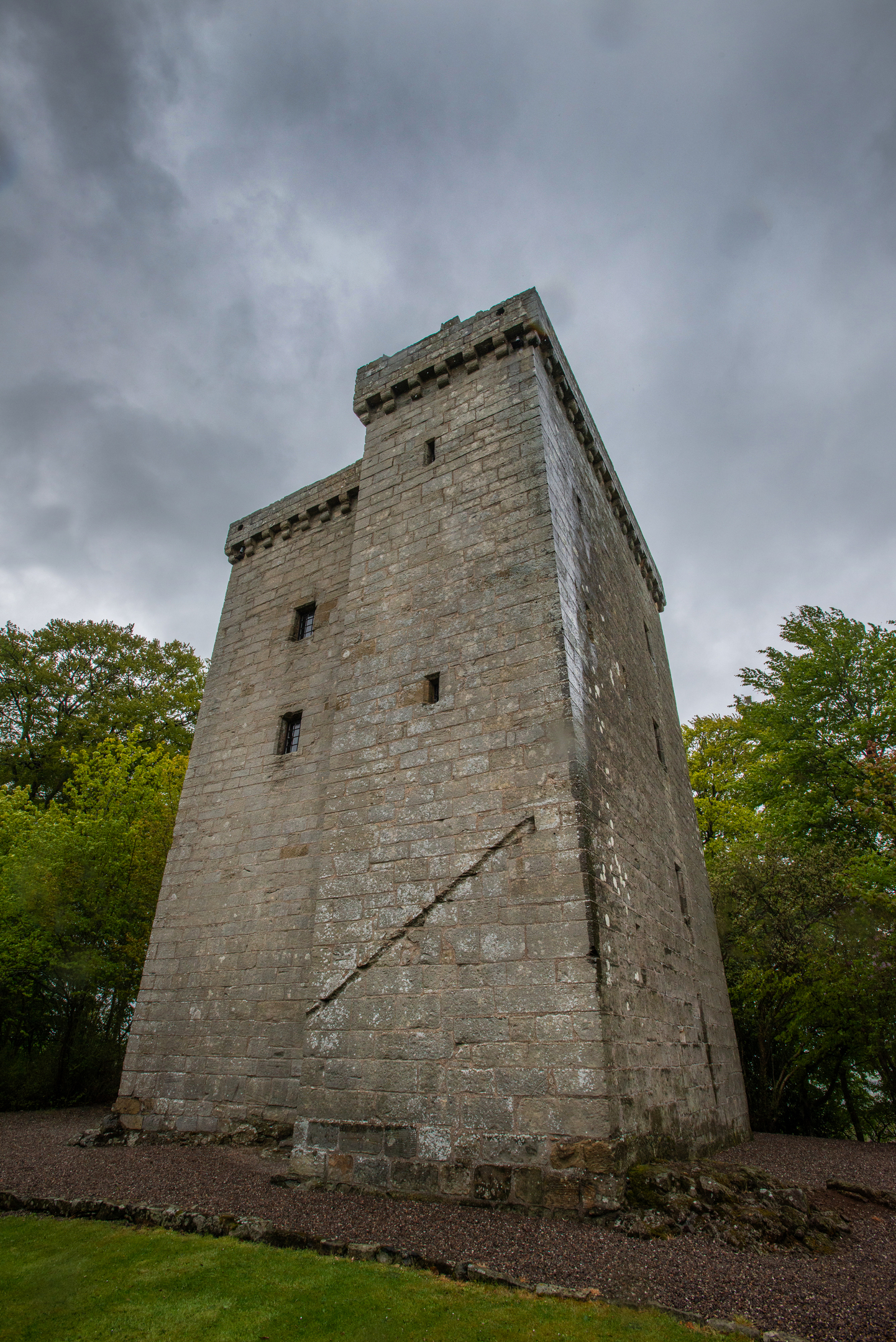 Looking up at the imposing stone walls of a tower house. There are very few windows, with none on the lower floors. 
